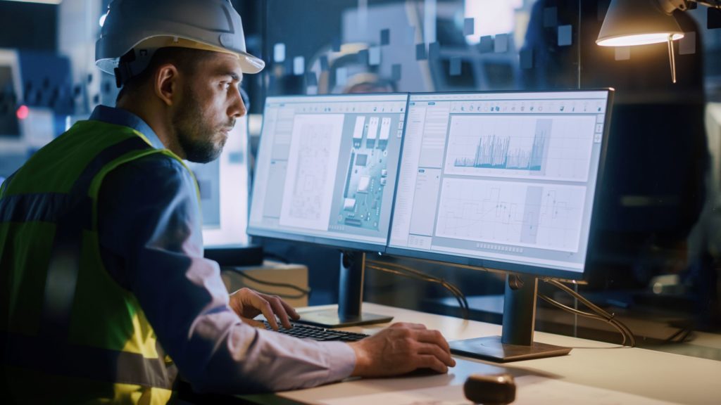 Male in hard hat using computer to look at graphs and charts